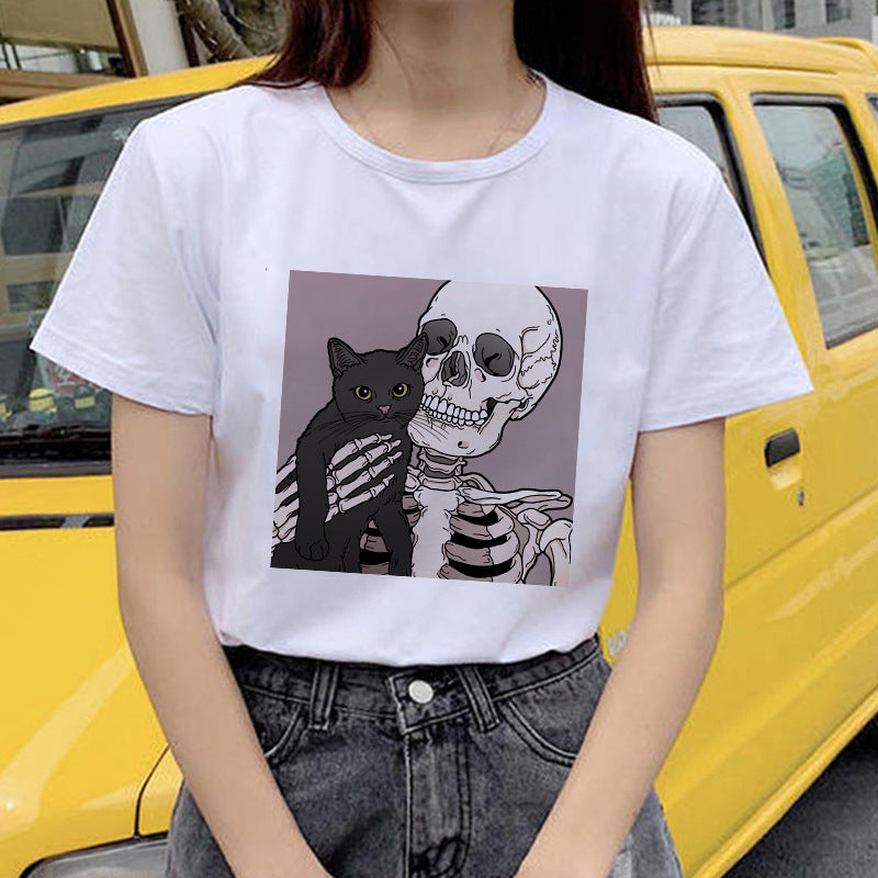 Person wearing a white t-shirt with a graphic design of a cat and skeleton, standing in front of a yellow vehicle.