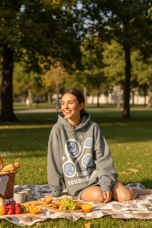 Person wearing a gray hoodie with a 'cosmic connection' design, holding a blue bag outdoors.